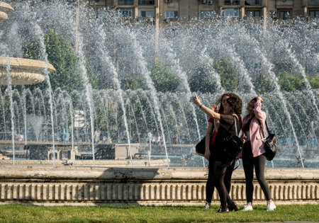 Bucharest/Romania - 05.30.2020:Three young girls taking a selfie in the Unirii Square, Bucharest, with the water fountains in the backgroundのeditorial素材