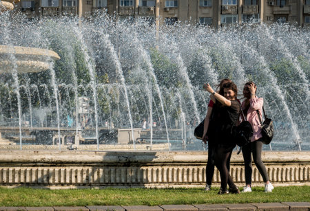 Bucharest/Romania - 05.30.2020:Three young girls taking a selfie in the Unirii Square, Bucharest, with the water fountains in the backgroundのeditorial素材