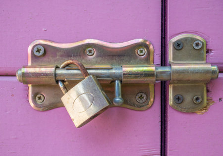 Close up with a locked purple door. Door latch with a rusty golden lock..