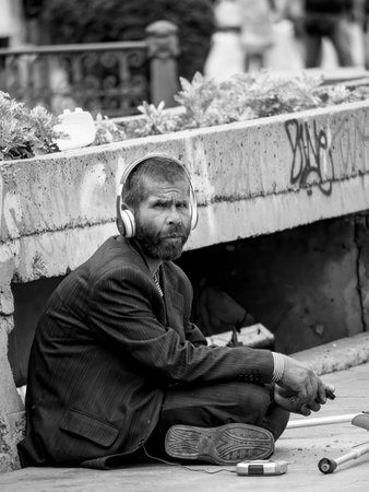 Bucharest/Romania - 07.25.2020: Homeless man or beggar sitting on the sidewalk and wearing headphones.のeditorial素材