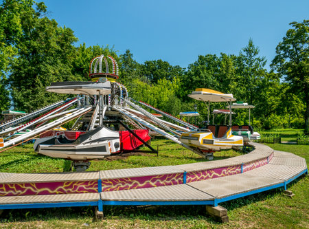 Amusement park ride machine and green trees against blue sky.のeditorial素材