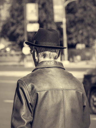 Vintage rear view of an old man wearing a leather jacket and a hat