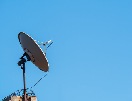 Satellite dish or parabolic antenna on the roof of a building against blue sky.の写真素材