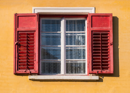 Detail of a window with old wooden shutters on a orange wall in medieval town of Sighisoara, Romania.の写真素材