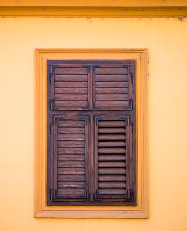 Detail of a window with old wooden shutters on a orange wall in medieval town of Sighisoara, Romania.の写真素材