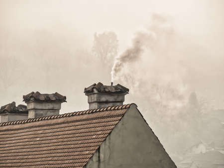 Rural landscape with smoke rising from the chimney of a house with old tiled red roofの写真素材