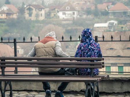 Couple sitting on a bench and admiring, from a belvedere point, the Sighisoara Citadel in Romania.