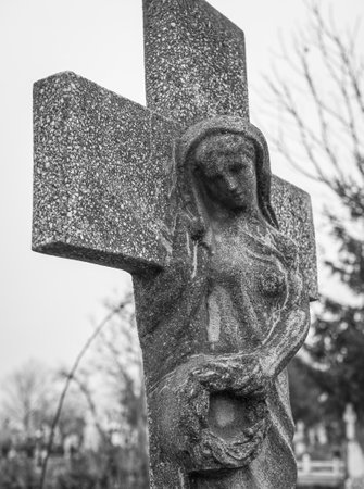 Virgin Mary mourning carved in a stone cross. Stone statue in a cemetery.の写真素材