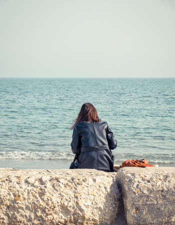 Girl sitting on a rock on the beach of the Black Sea and looking at the horizonの写真素材