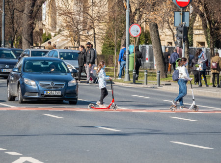 Two young girls crossing the street on electric scooters in Bucharest.のeditorial素材