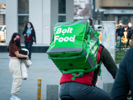 Bucharest, Romania - 03.17.2021: Bolt food courier on a bicycle carrying the green delivery bag. Young adult delivering the orderのeditorial素材