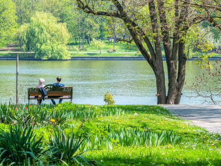 Couple sitting on a bench with a lake view in King Mihai I park( Herestrau), Bucharest Romania.の写真素材