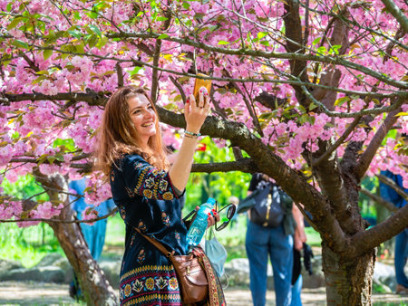 Bucharest, Romania - 04.29.2021: Beautiful attractive young girl taking a selfie under a cherry blossom tree in King Mihai I park (Herestrau).のeditorial素材