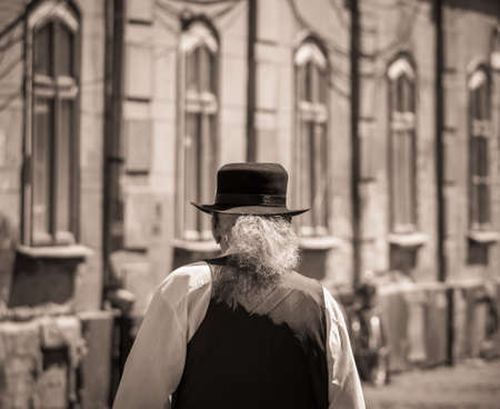 Old vintage sepia picture of a man with long gray hair and a black hat on his head. Back view of a senior man.の写真素材
