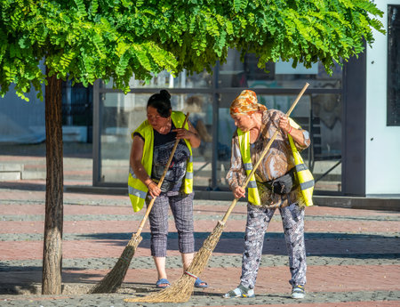 Timisoara, Romania - 06.20.2021: Two municipal female worker sweeping the pavement with broomstick, in the center of Timisoara.のeditorial素材