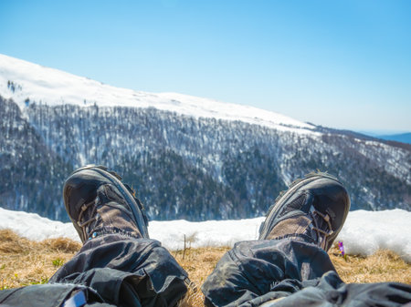 Hiker resting his feet after a long hike in the mountains.. Pair of hiking boots with Bucegi Mountains in the background. Winter landscape.の写真素材