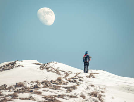 Winter landscape with a hiker taking a break to look at the bright moon aboveの写真素材