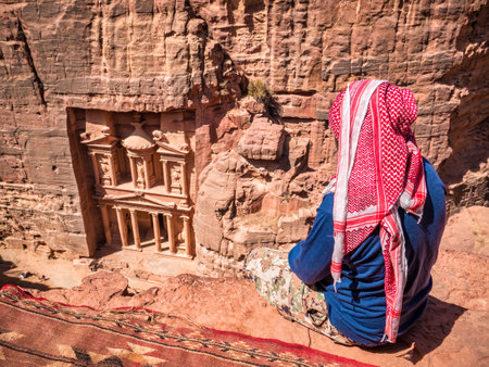 Local arab bedouin man looking at Al-Khazneh (The Treasury) one of the most elaborate temples in the ancient city of Petra, Jordan. View from above.の写真素材