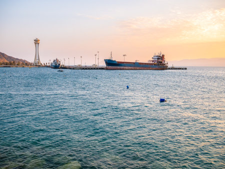 Scenic view at sunset with a docked old rusted ship and the lighthouse observation tower in the port of Aqaba city, Jordan.のeditorial素材