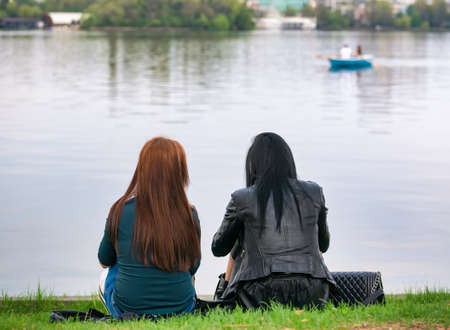 Rear view of two girls sitting on the edge of Herestrau lake in King Mihai I park, Bucharestの写真素材