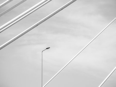 Abstract black and white picture with a isolated light pole and white metal bars of a suspended bridgeの写真素材