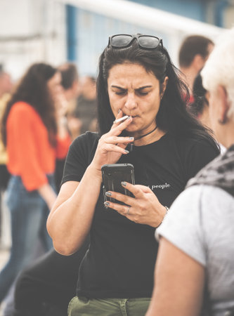 Bucharest, Romania -September 2022: Woman smoking a cigar and texting or browsing on her smartphone. Street photography in Bucharest.のeditorial素材