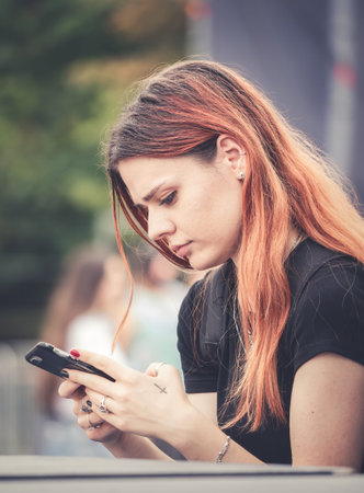Bucharest, Romania -September 2022: Beautiful red head girl browsing or texting on her smartphoneのeditorial素材