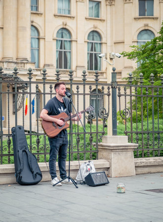 Bucharest, Romania - August 2022: Young street artist with a acoustic guitar playing in the center of Bucharest (Victory street - Calea Victoriei).のeditorial素材