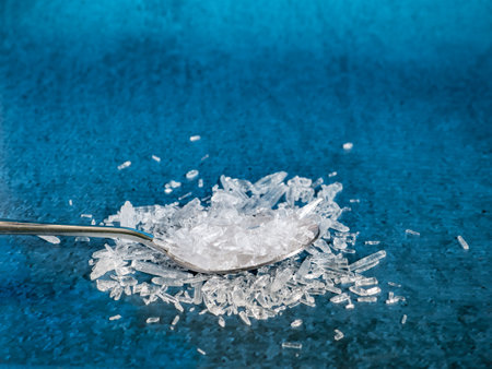 A metal spoon filled with natural menthol crystals on blue background.の写真素材