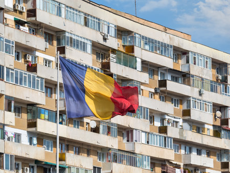 Romanian national flag in the wind and a worn out communist apartment building in the background, in Bucharest Romania.の写真素材