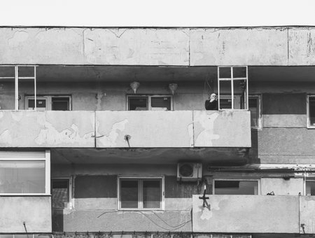 Bucharest, Romania - March 2023: Isolated man smoking a cigar in a balcony of a worn out communist apartment building in Bucharest.の写真素材