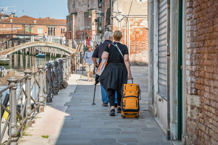 unidentifiable tourist woman with a luggage trolley walking near a water canal in Venice, Italy.の写真素材