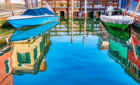 Picturesque colorful idyllic scene with a boat docked on the water canals in Burano Venice Italy. Water reflection.の写真素材