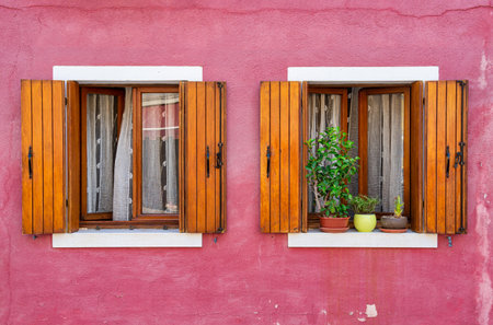 Detail with a colorful house windows with lots of flower pots and wooden shutters in Burano, Italy.の写真素材