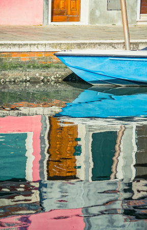 Picturesque colorful idyllic scene with a boat docked on the water canals in Burano Venice Italy. Water reflection.の写真素材