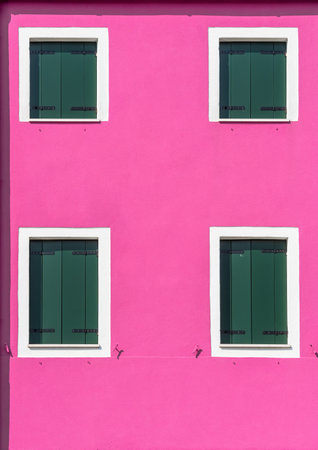 Detail with a pink colorful house window with green painted wooden shutters in Burano, Italy.の写真素材