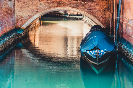 Picturesque scene from Venice with a boat docked or moored under a stone bridge on the narrow water canals.の写真素材
