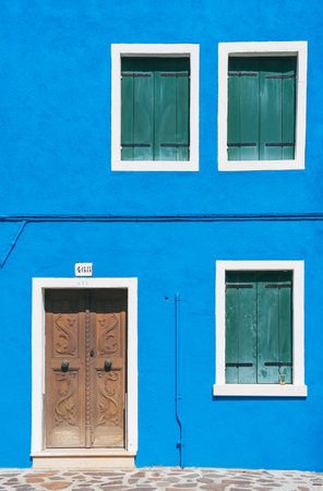 Detail with a colorful house windows and door entrance with blue painted wall and wooden shutters in Burano, Italy.のeditorial素材