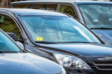 Small yellow beginner driver sign sticker on the windshield of a parked car.の写真素材