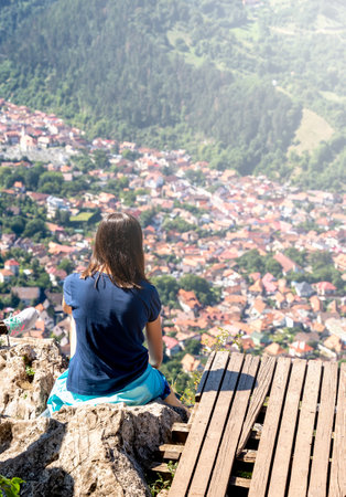 Rear view with a unidentifiable brunette young tourist girl enjoying the view from the belvedere point on Mount Tampa over Brasov city, Romania.の写真素材