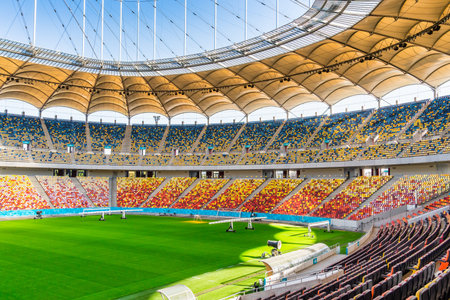 Empty stadium with colored chairs in tribune and the green lawn grass. The National Arena stadium in...