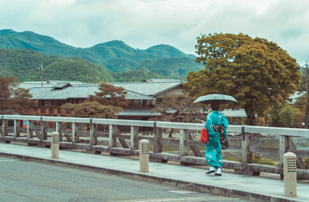 Picturesque scene with a woman holding an umbrella and wearing a traditional japanese kimono on the Togetsukyo Bridge in Arashiyama, Kyoto.の写真素材