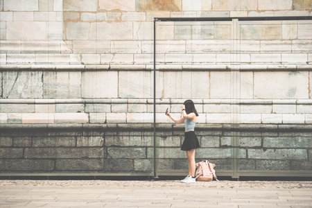 A unidentifiable young girl taking a selfie next to the walls of Duomo di Milano Cathedralの写真素材