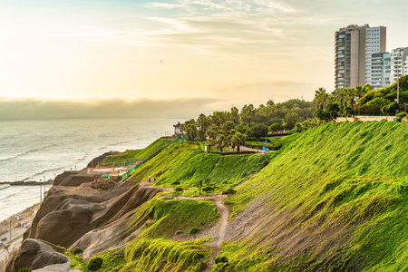 A scenic view of a lush green clifftop park in the Miraflores district of Lima, Peru. People strolling along coastal walkway at sunset.の写真素材