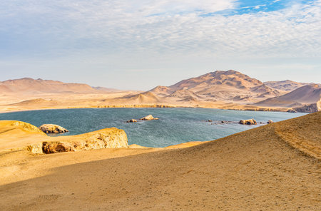 View of the arid desert landscape meeting the deep blue Pacific Ocean at Paracas National Reserve in Peru.の写真素材