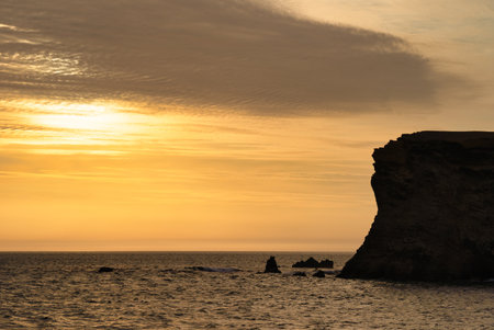 Golden sunset behind dramatic coastal cliffs in Paracas National Reserve, Peru. Pacific ocean landscape at dusk.の写真素材