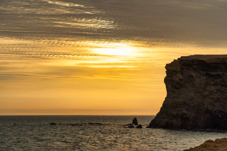 Golden sunset behind dramatic coastal cliffs in Paracas National Reserve, Peru. Pacific ocean landscape at dusk.の写真素材