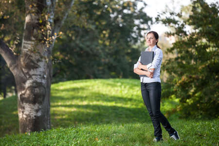 Mature woman holding a aptop in her arm walking in the parkの写真素材