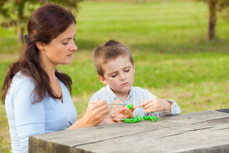 Young woman teacher teaches little young boy in white shirt painting with the brush to make artisanal pasta beadsの写真素材