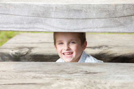 white little boy hiding under the wooden tableの写真素材